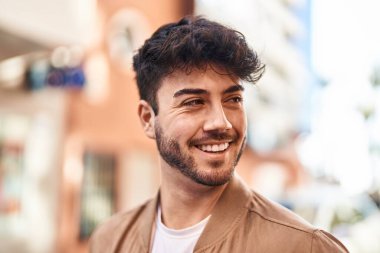 Young hispanic man smiling confident looking to the side at street