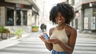 Sokakta gülümseyen akıllı telefon kullanan Afrikalı Amerikalı kadın.