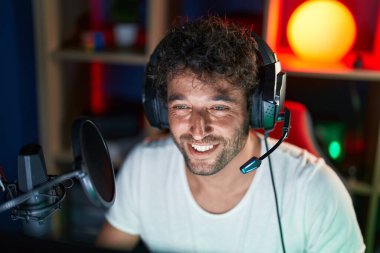 Genç İspanyol asıllı, gülümseyen, kendine güvenen, müzik stüdyosundaki masada oturan.