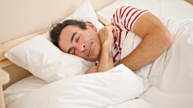 Orta yaşlı bir adam yatakta uzanıyor, yatak odasında uyuyor.
