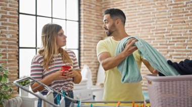 Kadın ve erkek çamaşır ipine asılmış çamaşırhanede kahve içiyorlar.