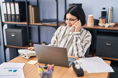 Genç Çinli iş kadını ofiste telefonla konuşuyor.