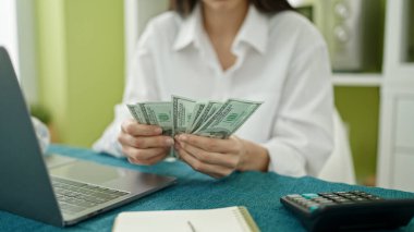 Genç ve güzel İspanyol kadın yemek odasında deftere dolar sayıyor.