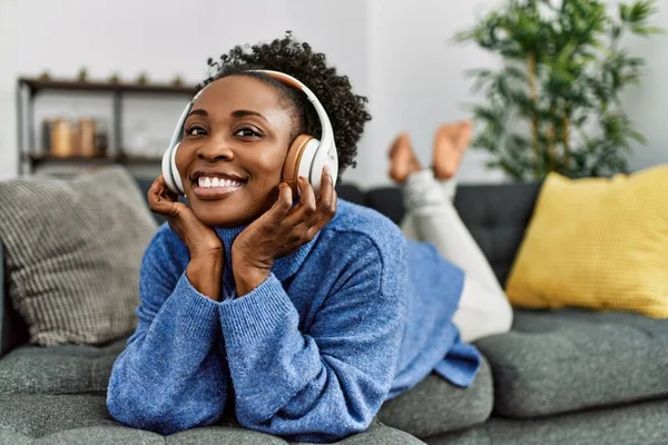 African american woman listening to music lying on sofa at home