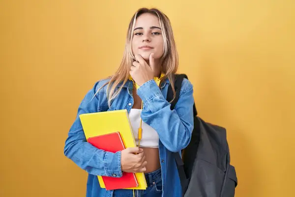 Młoda Blondynka Nosząca Studencki Plecak Trzymająca Książki Wyglądająca Pewnie Przed — Zdjęcie stockowe