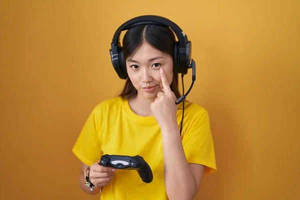 中国的年轻女子拿着游戏控制器指着你的眼睛看着你的手势 怀疑的表情 — 图库照片