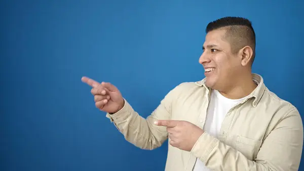 Jonge Latino Man Glimlachend Zelfverzekerd Wijzend Naar Zijkant Geïsoleerde Blauwe — Stockfoto