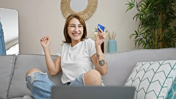 自宅で祝うソファに座っているラップトップとクレジットカードで買い物をする若い女性 — ストック写真