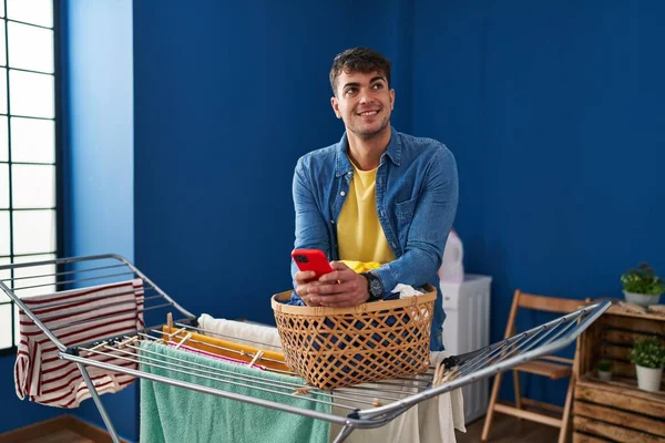 Ung Latinamerikan Man Med Smartphone Hängande Kläder Klädstreck Tvättstuga — Stockfoto