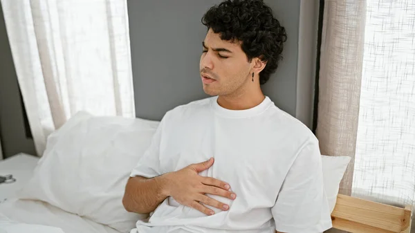 Young latin man sitting on sofa suffering anxiety attack at bedroom