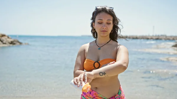 若い美しいヒスパニック女性観光客はビーチで日焼け止めを塗るビキニを着ています — ストック写真