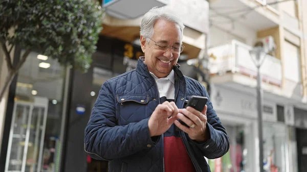 Sokakta gülümseyen akıllı telefon kullanan gri saçlı orta yaşlı bir adam.