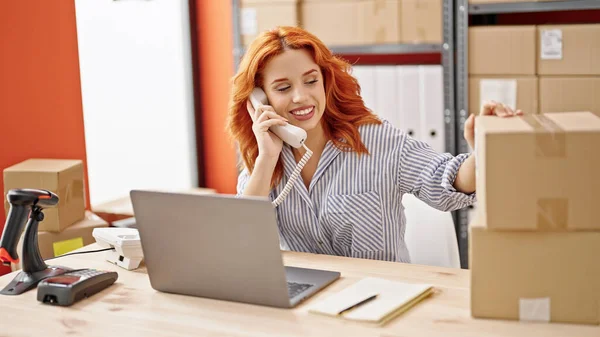 年轻的红头发女性电子商务工作者在办公室使用笔记本电脑在电话中交谈 — 图库照片