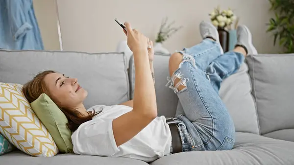 自宅のソファーに横になっているスマート フォンを使用して若い女性 — ストック写真