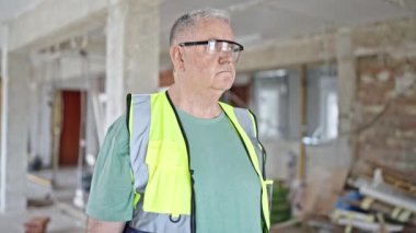 İnşaat alanında gevşek bir ifadeyle duran orta yaşlı gri saçlı adam müteahhit.