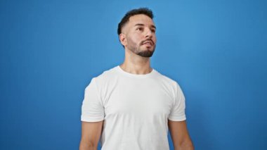 Genç Arap adam, izole edilmiş mavi arka planda kameraya işaret eden birini arıyor.