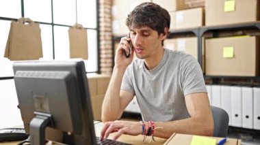 İspanyol asıllı genç iş adamı bilgisayarda daktilo yazıp ofisteki akıllı telefondan konuşuyor.