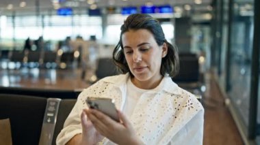 Havaalanında gülümseyen akıllı telefon kullanan güzel bir İspanyol kadın.