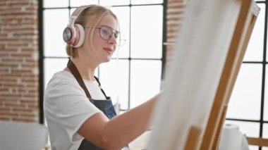 Sanat stüdyosunda müzik dinleyen genç sarışın kadın sanatçı.