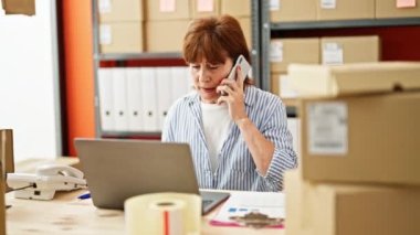 Orta yaşlı kadın ecommerce iş işçisi. Ofiste bilgisayarla akıllı telefondan tartışıyor.