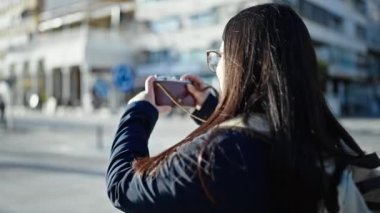 Sırt çantalı genç İspanyol kadın turist sokakta kamerayla fotoğraf çekiyor.
