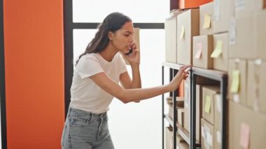 Afro-Amerikalı kadın ekommerce işçisi akıllı telefondan konuşuyor ofiste raflarda paket arıyor.