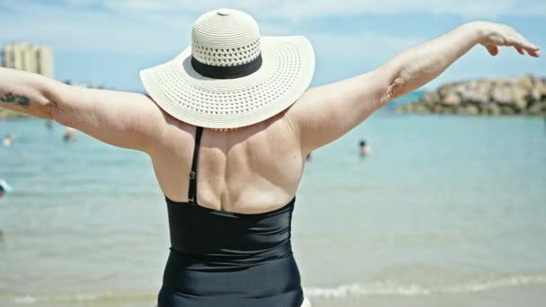 中世の灰色の髪の女性観光客は ビーチで腕を伸ばす水着を着て自信を持って微笑みます — ストック動画
