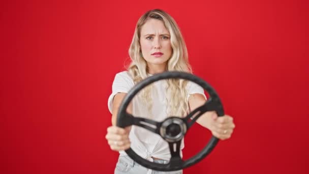 ドライバーとしてステアリングホイールを使用している若い金髪の女性は 孤立した赤い背景に強調 — ストック動画