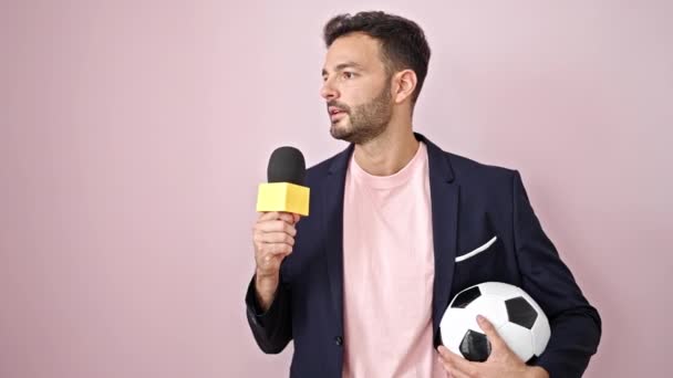 Young hispanic man soccer reporter doing interview speaking over isolated pink background