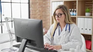 Klinikte bilgisayar kullanan genç sarışın kadın doktor.