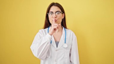 Genç, güzel İspanyol kadın doktor izole edilmiş sarı arka planda sessizlik istiyor.