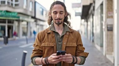 Genç İspanyol adam sokakta gülümseyen akıllı telefon kullanıyor.