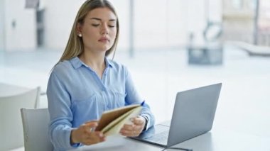 Genç sarışın iş kadını ofiste dizüstü bilgisayar okuyarak çalışıyor.