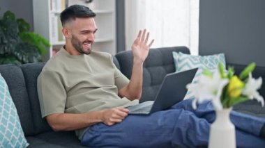 Evdeki kanepede oturan Latin asıllı genç bir adam.