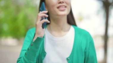 Parkta gülümseyen akıllı telefondan konuşan genç Çinli kadın.