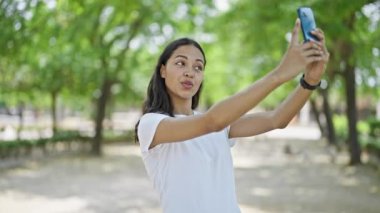 Afro-Amerikalı kadın, parkta akıllı telefonun yanında kendinden emin bir şekilde selfie çekiyor.