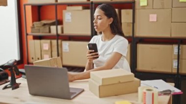 Afrikalı Amerikalı kadın dış ticaret işçisi ofisteki akıllı telefonla paketlere fotoğraf çekiyor.