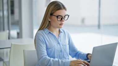 Ofiste çalışan genç sarışın iş kadını dizüstü bilgisayar kullanıyor.