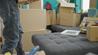 Genç İspanyol adam yeni evinde sırt ağrısı çektiği için paketi kanepeye koyuyor.