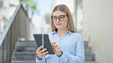 Genç sarışın iş kadını sokak ortasında müzik dinliyor.