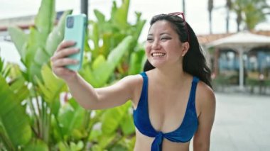 Bikini giyen Çinli genç bir turist parkta video görüşmesi yapıyor.