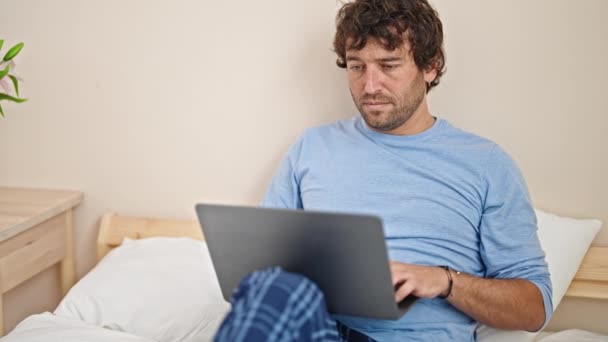 Ung Latinamerikan Man Efterbehandling För Att Använda Laptop Sitter Sängen — Stockvideo