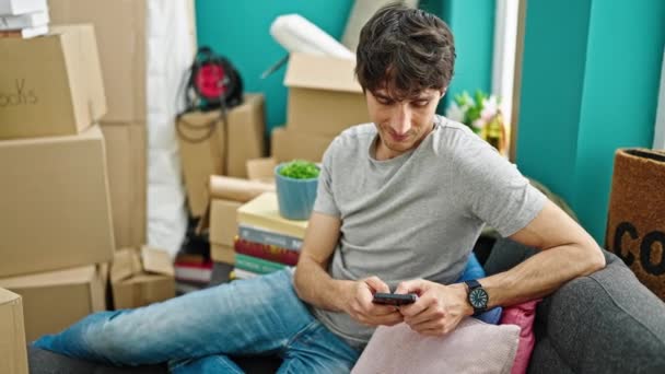 Joven Hombre Hispano Usando Smartphone Sentado Sofá Celebrando Nuevo Hogar — Vídeos de Stock