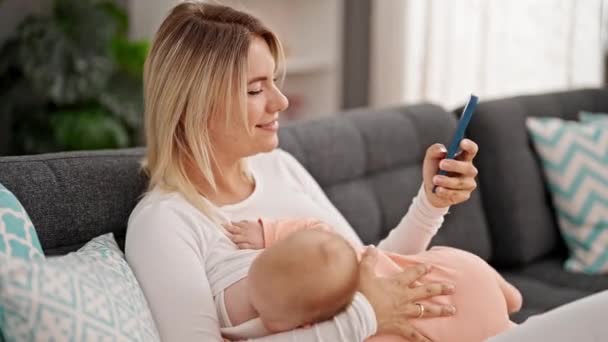 Μητέρα Και Κόρη Κάθονται Στον Καναπέ Θηλάζοντας Μωρό Χρησιμοποιώντας Smartphone — Αρχείο Βίντεο