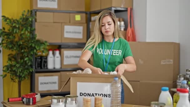 Молодая Блондинка Волонтер Улыбается Уверенно Упаковывая Одежду Пожертвования Благотворительном Центре — стоковое видео