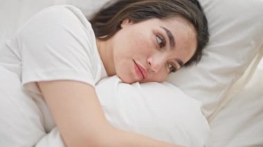 Young beautiful hispanic woman lying on bed with serious expression at bedroom