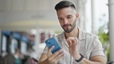 Young hispanic man smiling confident making selfie by the smartphone at coffee shop terrace
