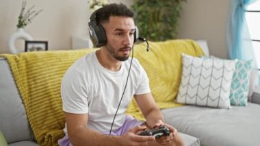 Genç Arap adam video oyunu oynuyor. Evdeki kanepede oturuyor.