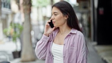 Genç, güzel, İspanyol bir kadın gülümsüyor ve caddede akıllı telefondan konuşuyor.