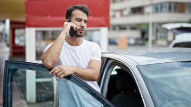 Genç İspanyol adam akıllı telefondan konuşuyor. Sokakta arabaya yaslanıyor.